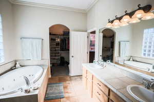 Full bath with a whirlpool tub, a spacious closet, double vanity, crown molding, and light tile patterned floors