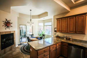Kitchen featuring a raised ceiling, stainless steel dishwasher, dark stone countertops, decorative light fixtures, and a peninsula