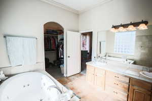 Bathroom featuring a whirlpool tub, double vanity, a spacious closet, ornamental molding, and light tile patterned floors