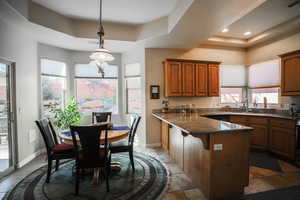 Kitchen with a raised ceiling, plenty of natural light, dark stone counters, and brown cabinetry