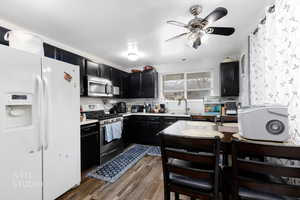 Kitchen with dark cabinetry, appliances with stainless steel finishes, light countertops, dark wood-style floors, and a ceiling fan