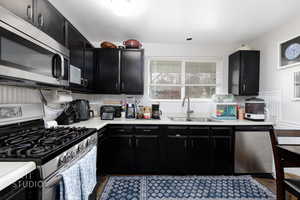 Kitchen with dark cabinets, stainless steel appliances, light countertops, and a wainscoted wall