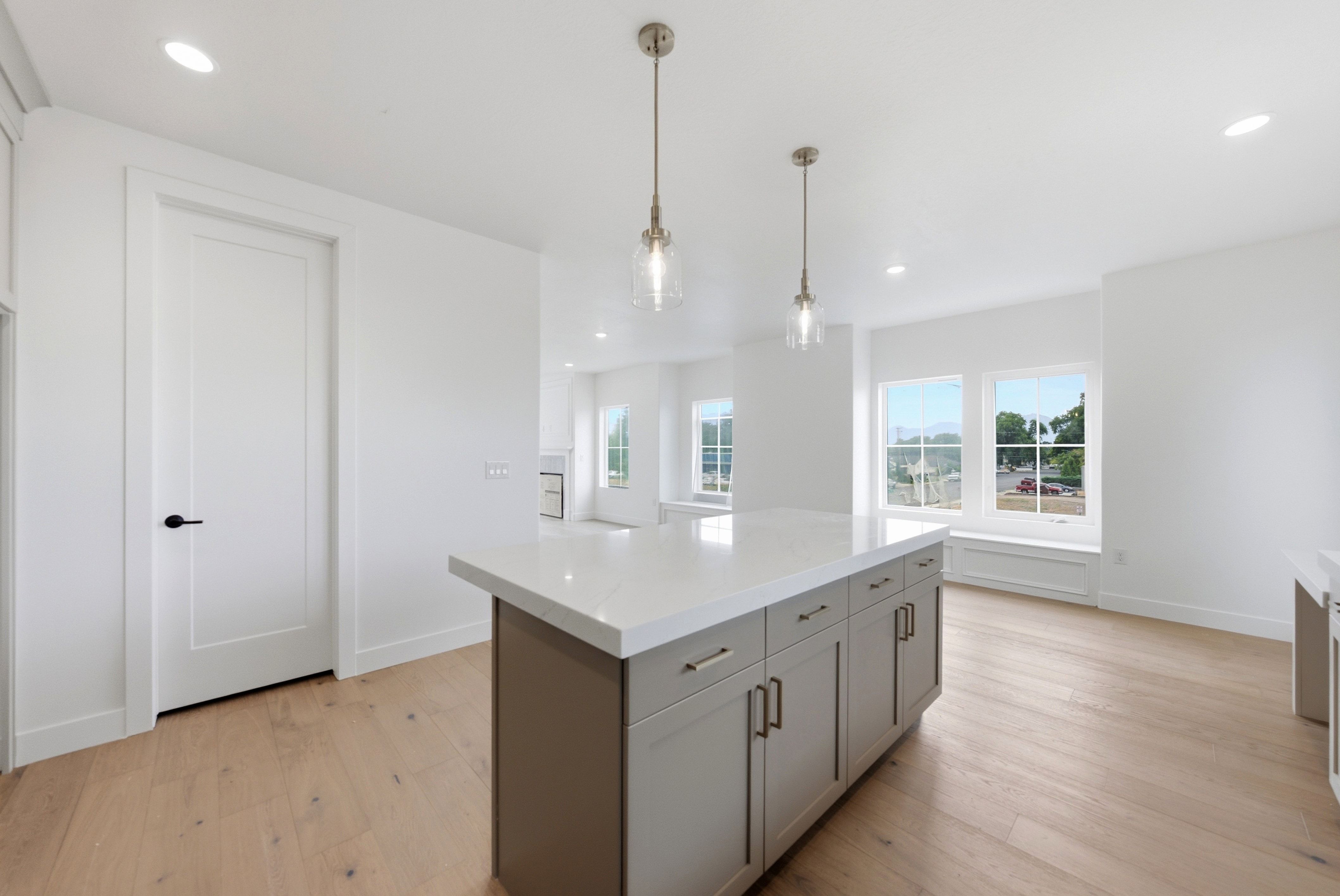 Kitchen island with a light-toned countertop and grey cabinetry, illuminated by two pendant lights and recessed lighting