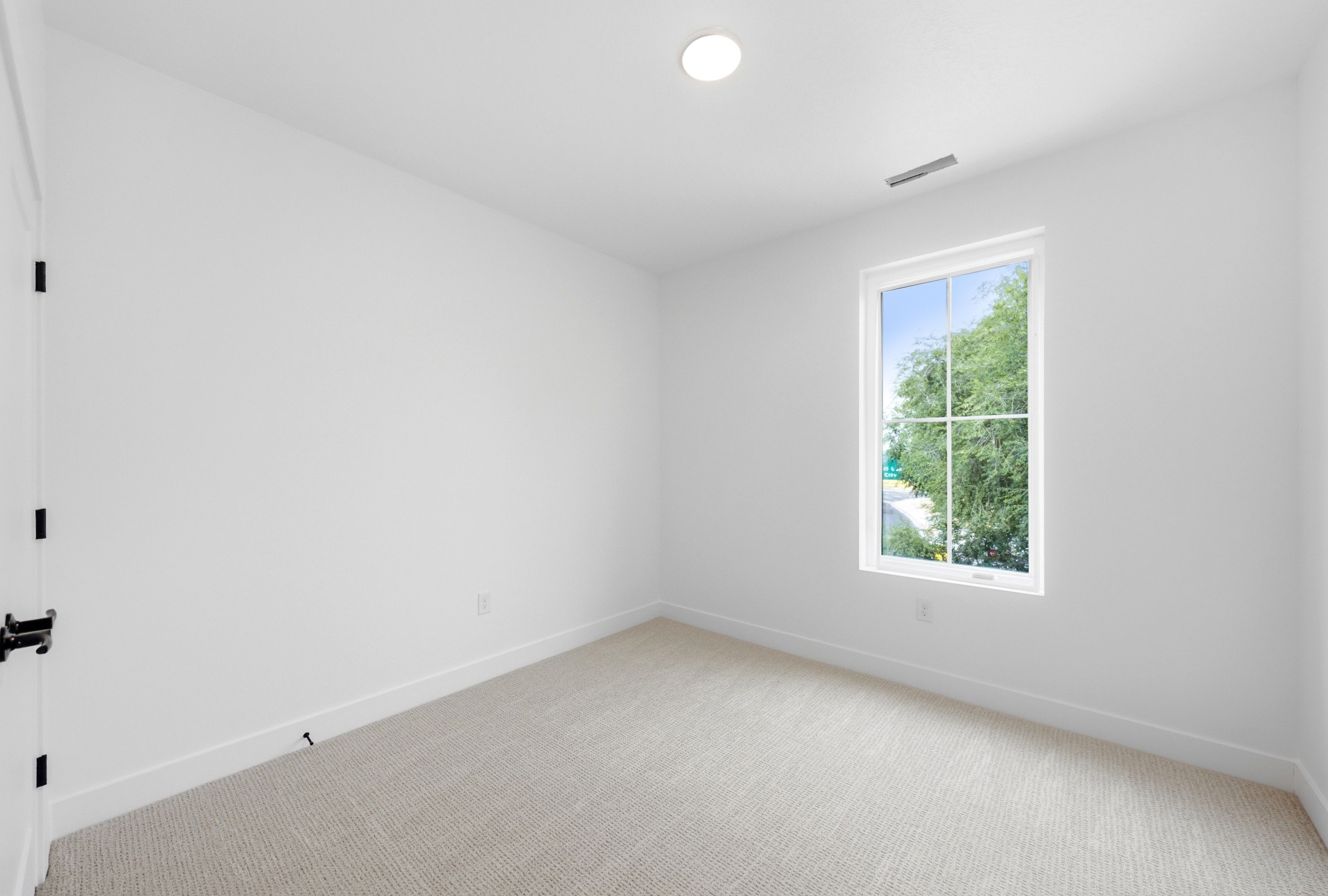Room with crisp white walls and neutral carpeting, featuring a single window with grids overlooking greenery