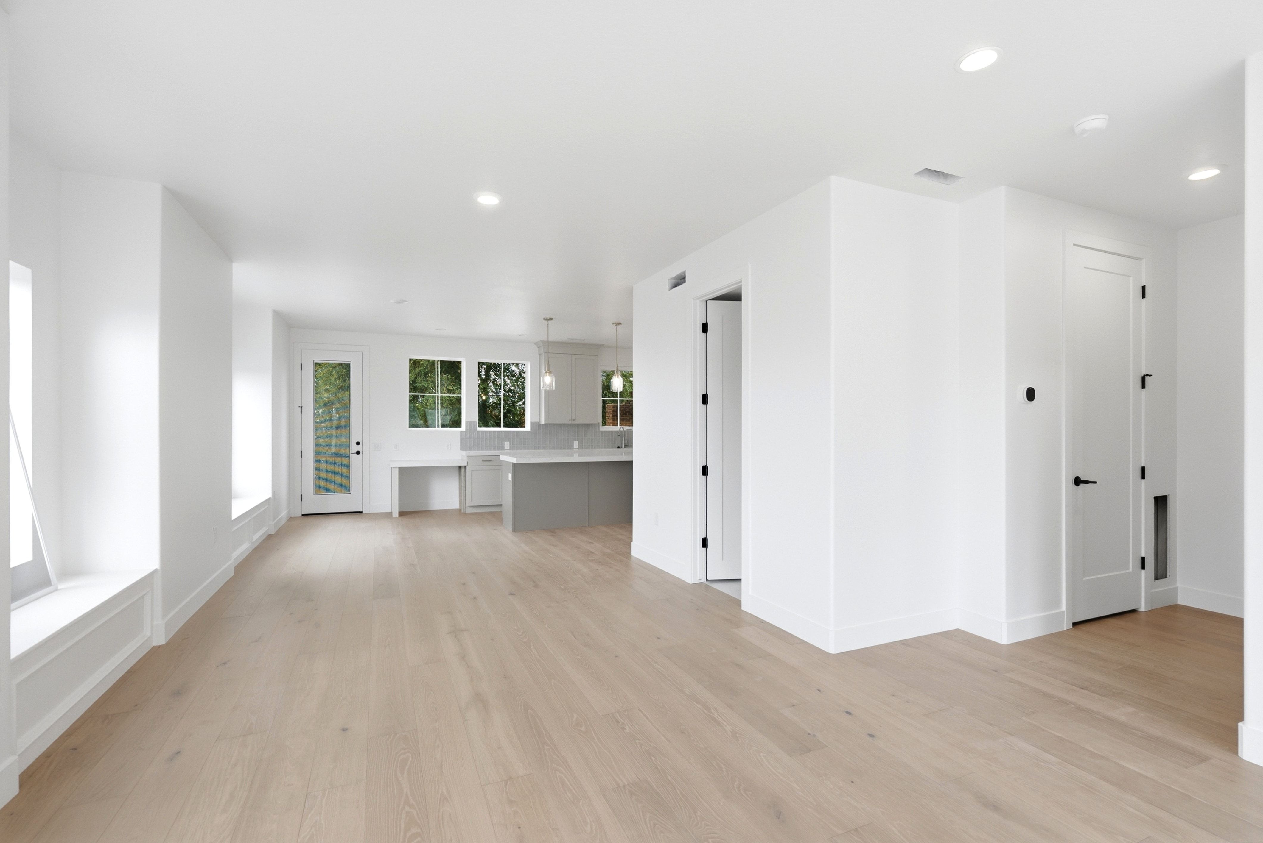 Bright open-concept living area featuring light wood-finish flooring, recessed lighting, and white walls
