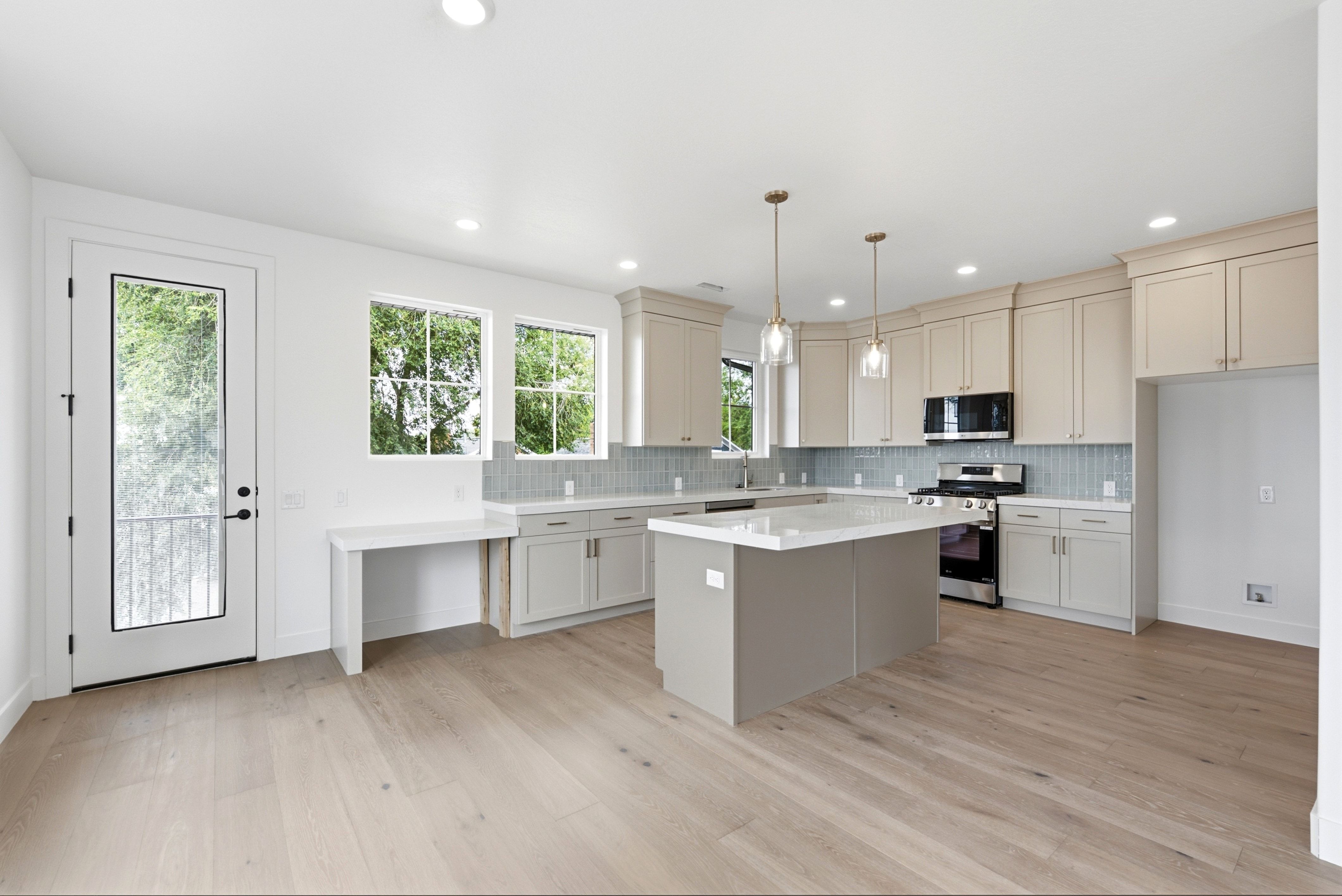 Spacious kitchen featuring light wood-finish flooring, a central island with a white countertop, extensive light cabinetry, a full tile backsplash, and stainless steel appliances