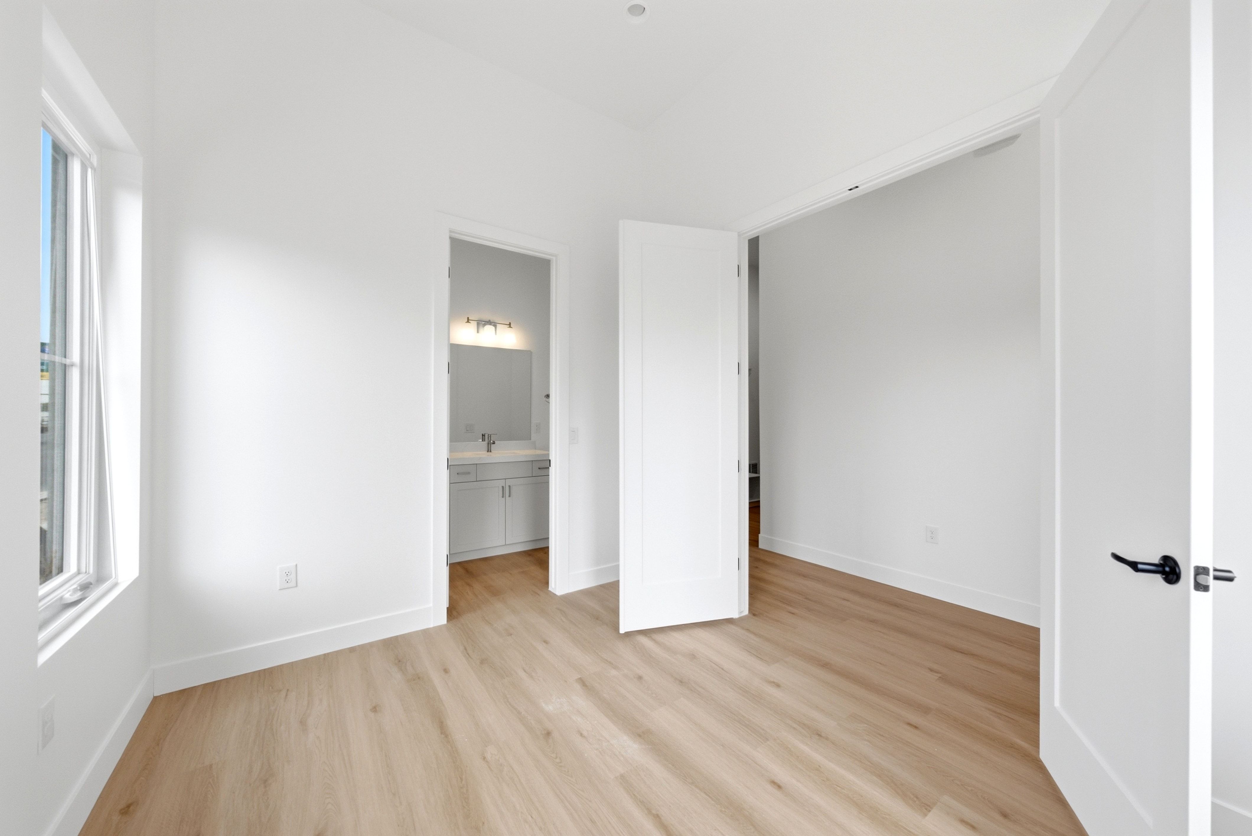 Room featuring wood-finish flooring, white walls, and a window with white trim