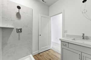 Full bathroom with vanity, a marble finish shower, and light wood-style floors