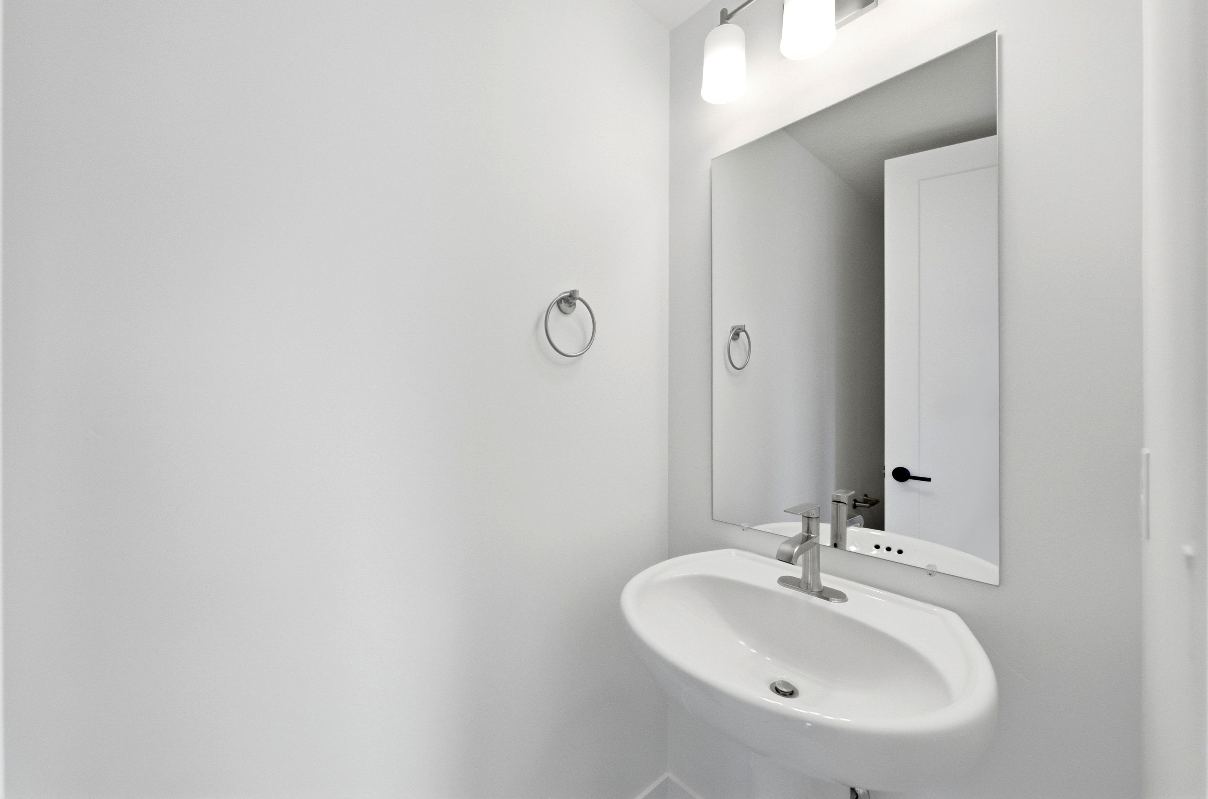 Pedestal sink featuring a chrome faucet, large frameless mirror, and a two-light vanity fixture with conical shades