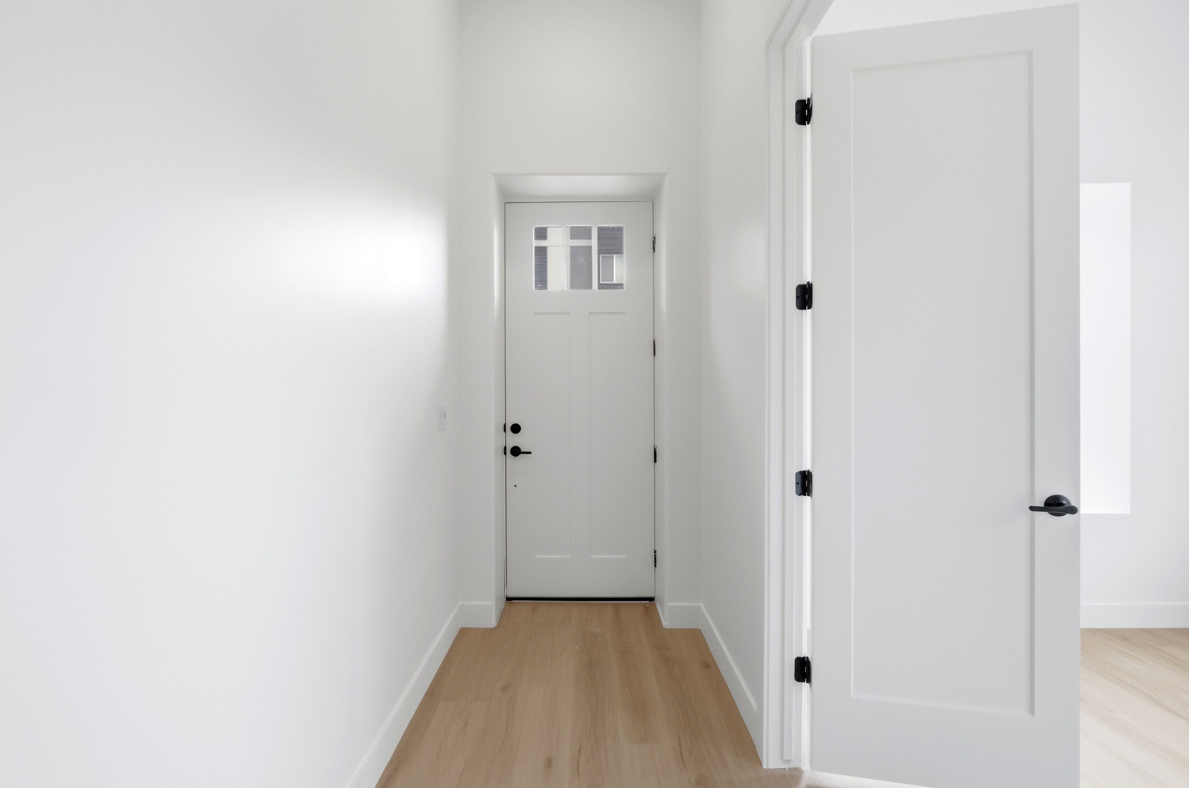 Entryway featuring a white paneled door with frosted glass inserts, wood-finish flooring, white baseboards, and matte black hardware