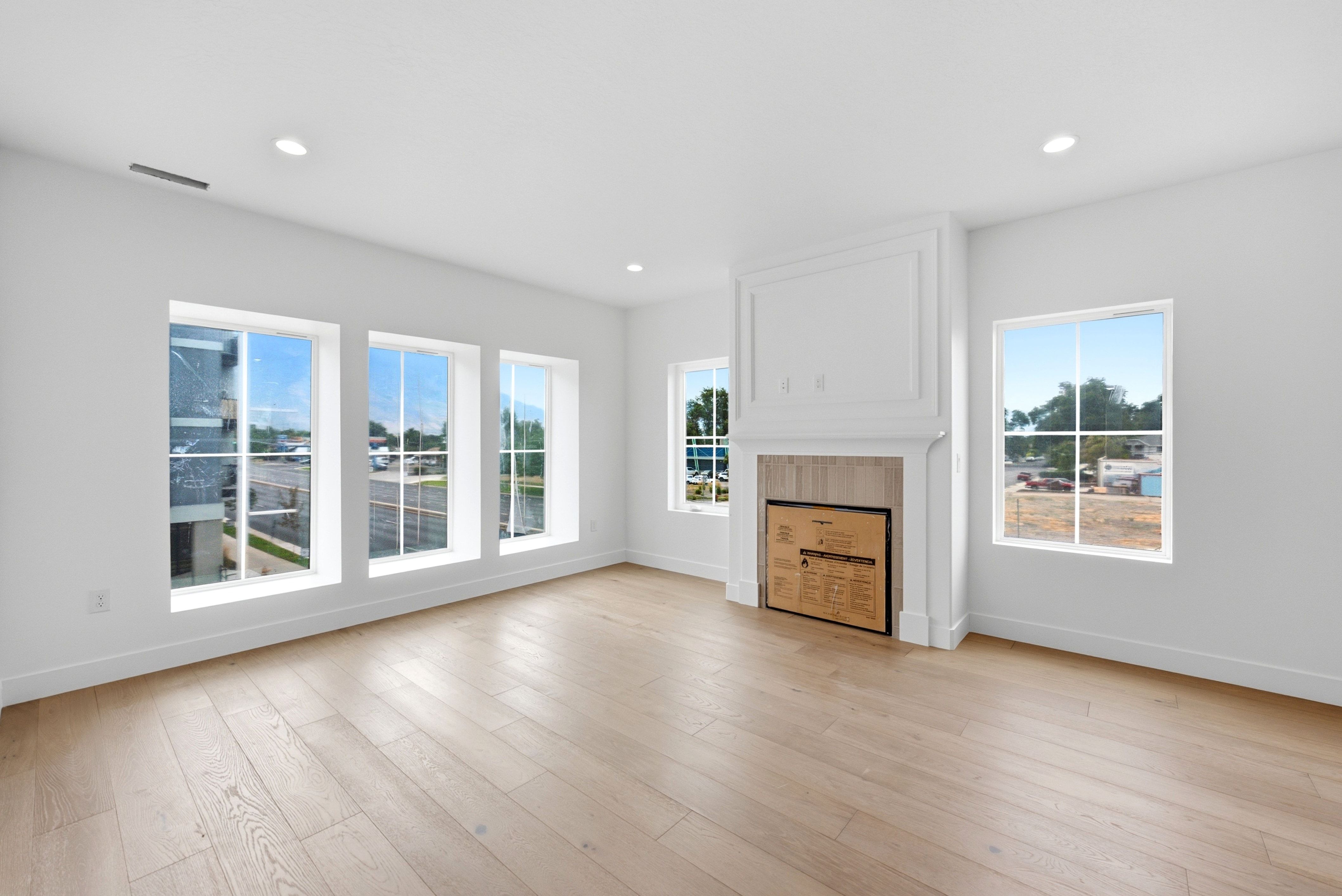 Spacious room featuring wood-finish flooring, a built-in fireplace with a decorative mantel, multiple large windows, recessed lighting, and white baseboards