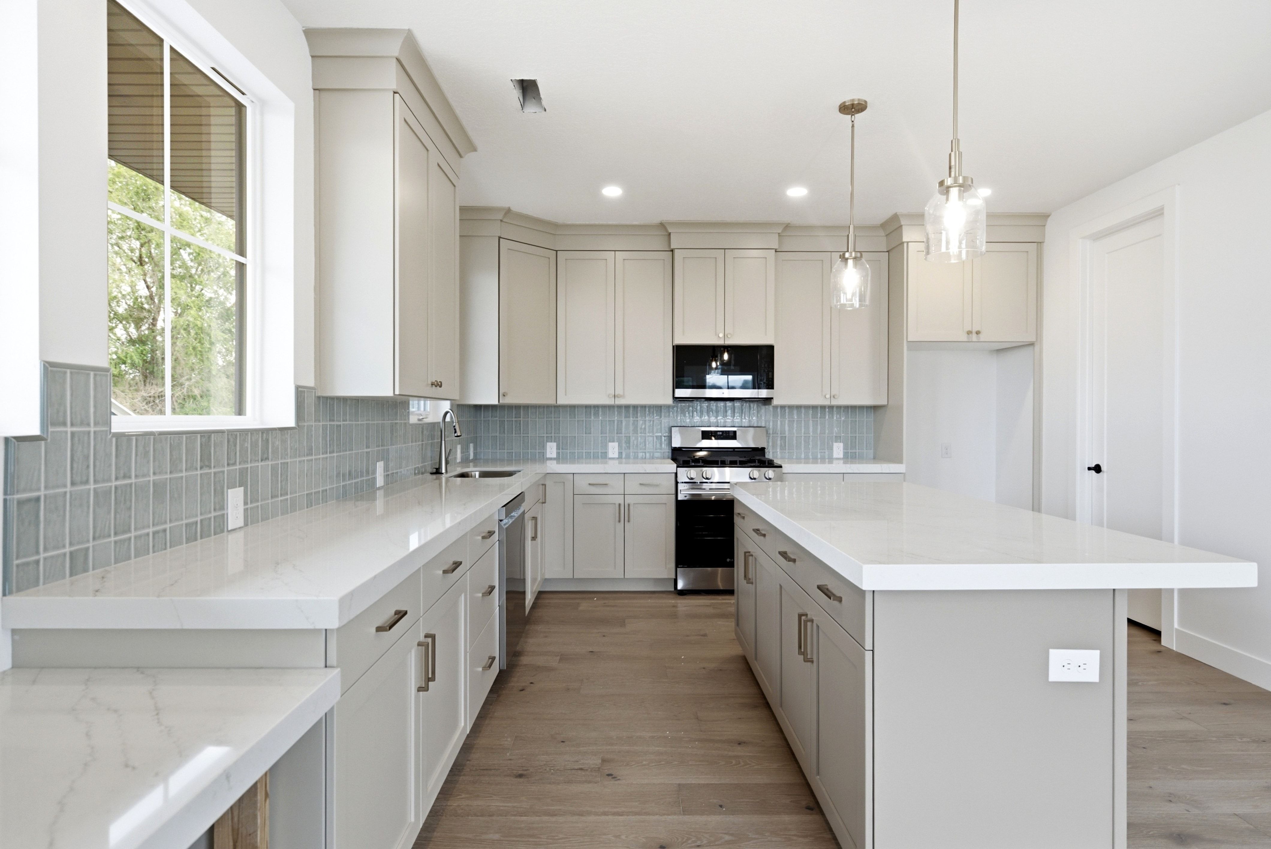 Kitchen featuring wood-finish flooring, light cabinetry, white countertops, tile backsplash, and stainless steel appliances