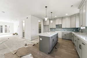 Kitchen with gray cabinetry, a center island, light stone counters, tasteful backsplash, and hanging light fixtures