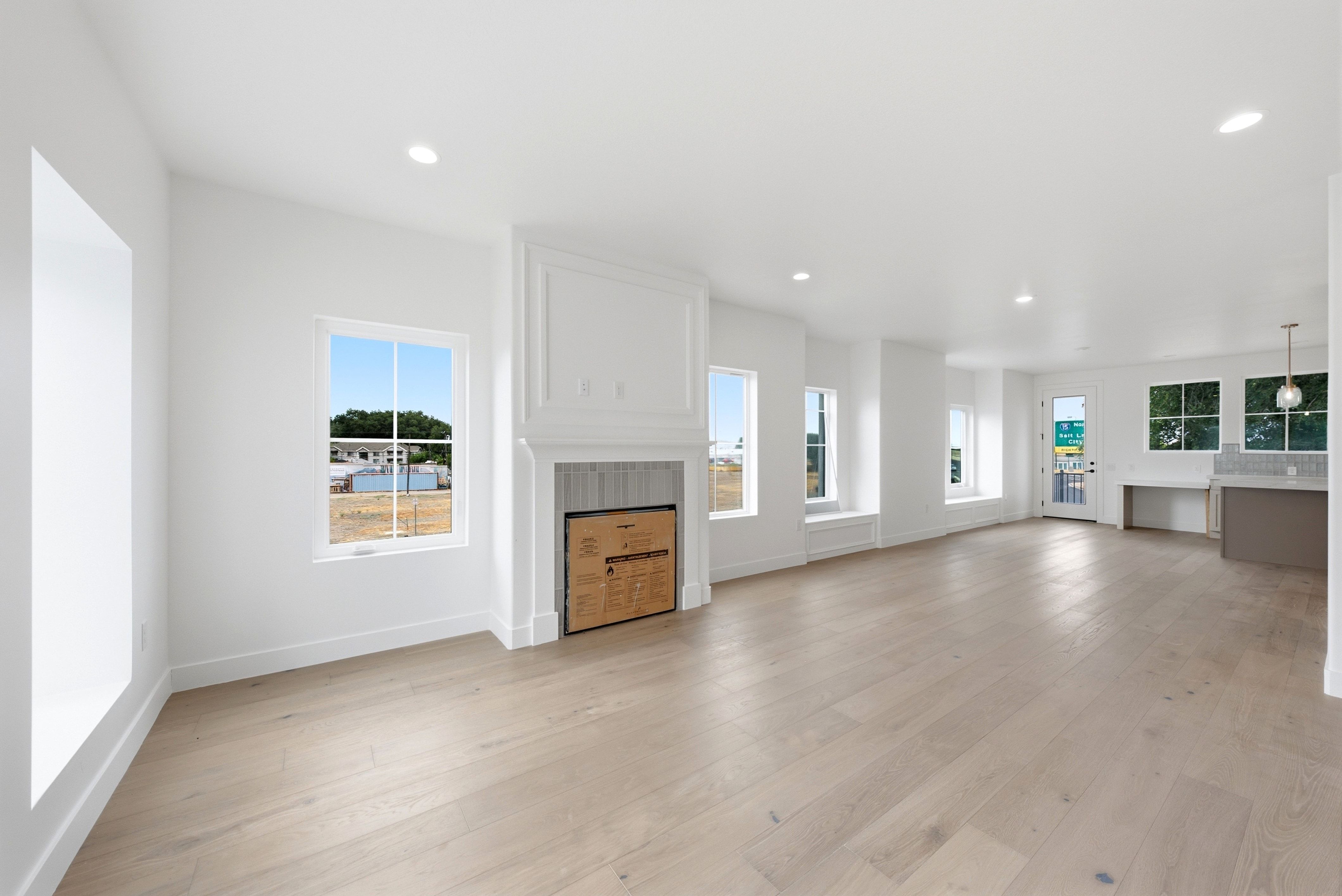 Expansive living area with light wood-finish flooring, recessed lighting, and a prominent fireplace with decorative molding