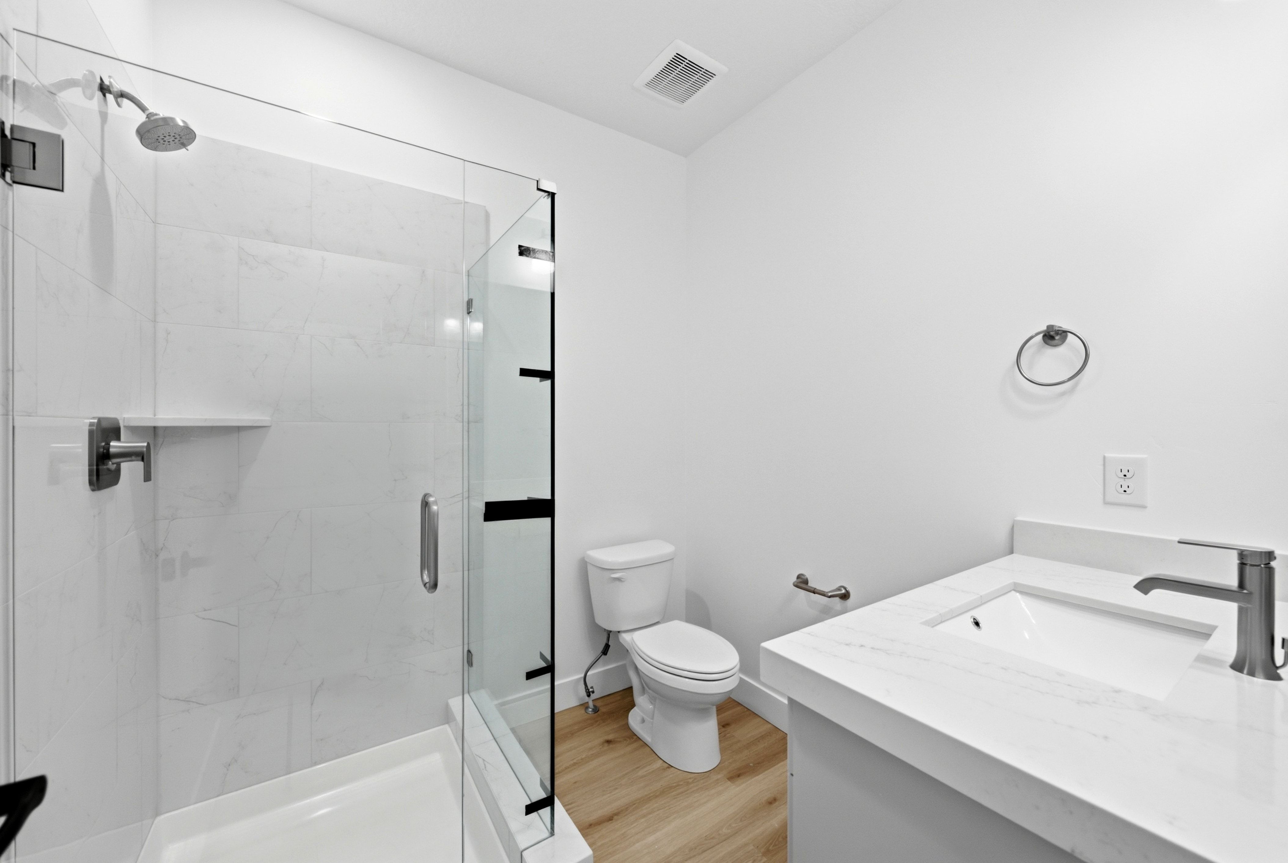 Contemporary bathroom featuring a glass-enclosed shower with white tiled walls, a built-in shower shelf, a white toilet, a vanity with a white countertop and integrated sink, and wood-finish flooring