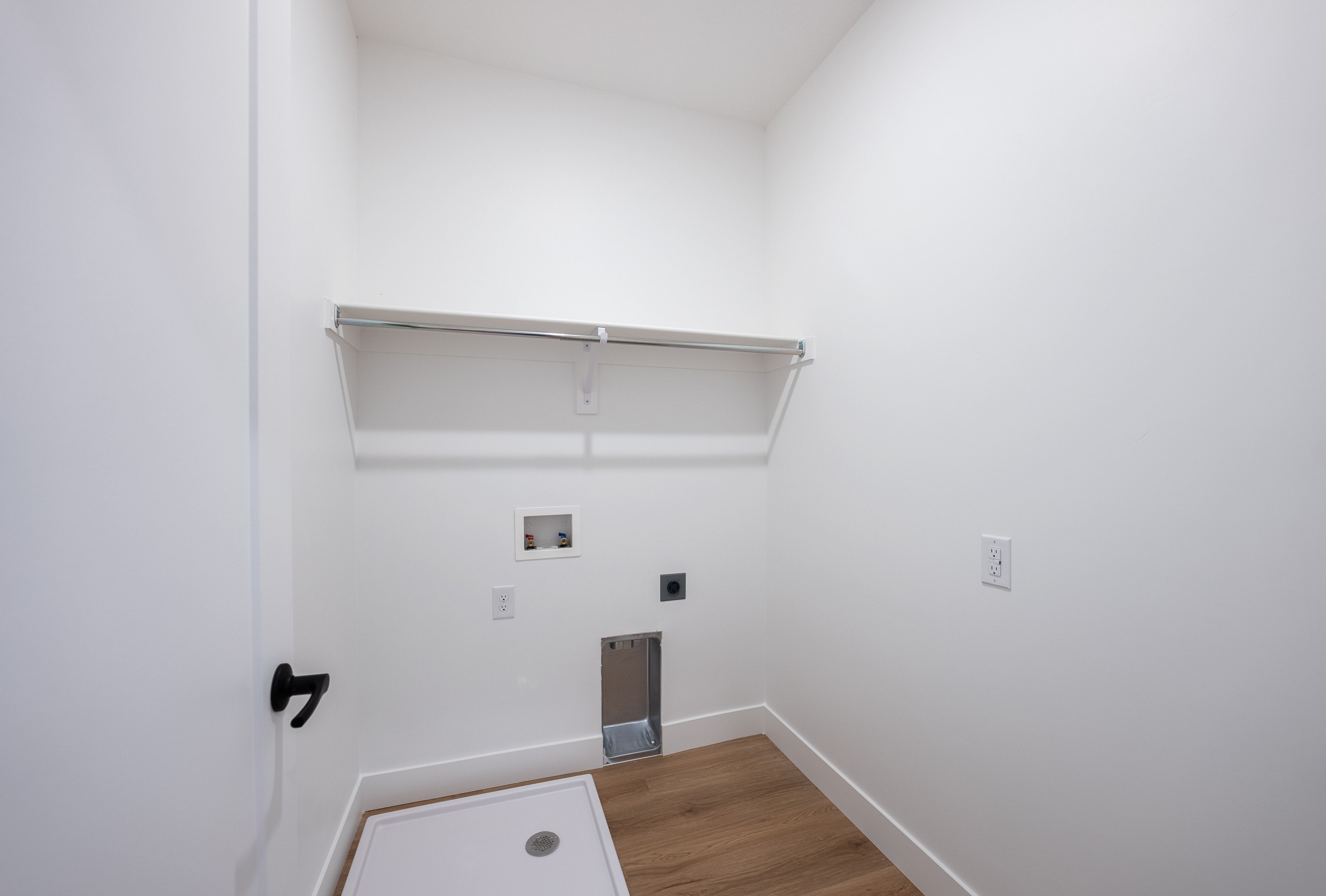 Dedicated utility space featuring a chrome hanging rod, white shelving, and wood-finish flooring