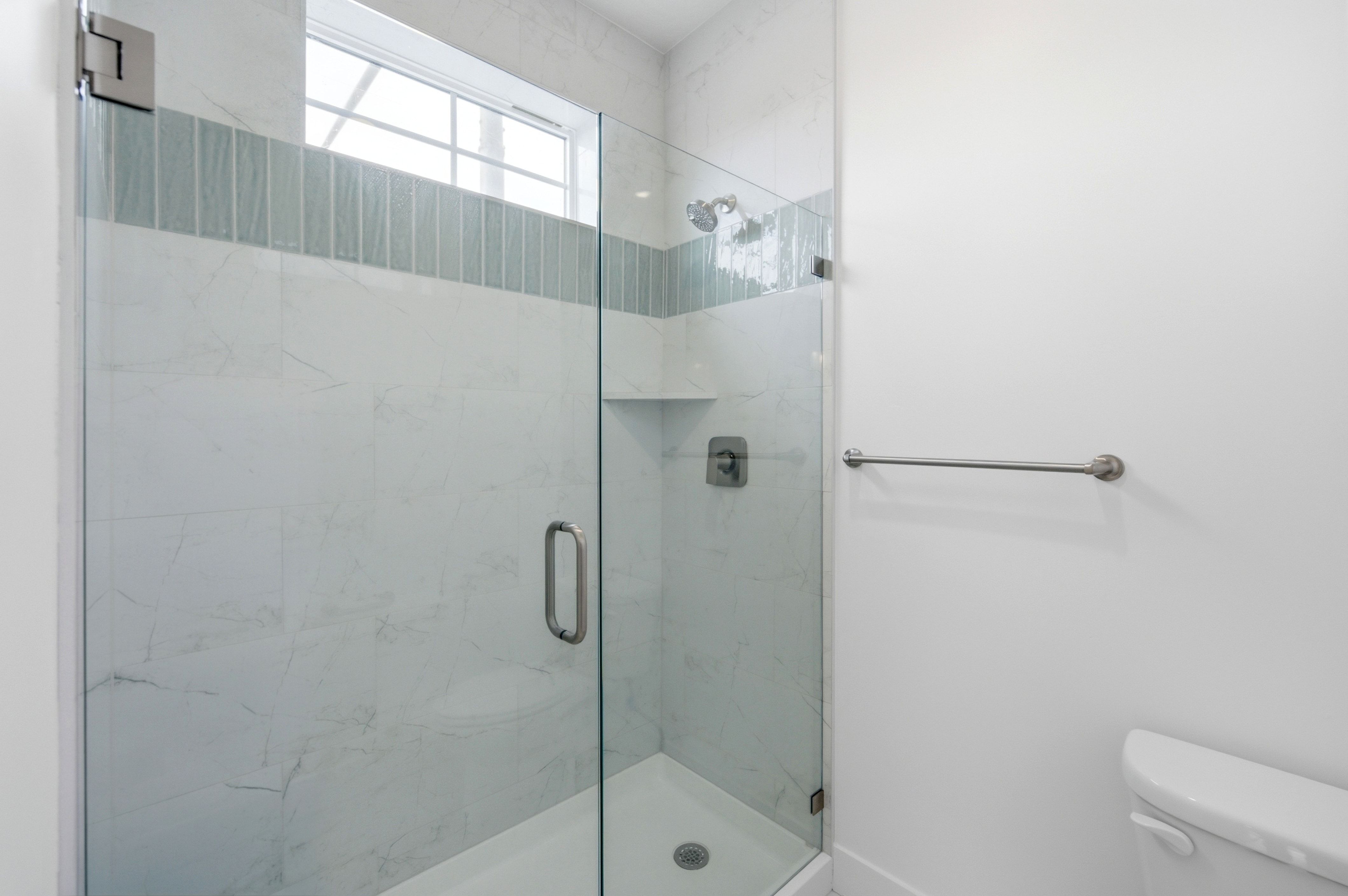 Glass-enclosed shower with white marble-look tile walls, a decorative accent band, built-in shelving, and a chrome shower fixture