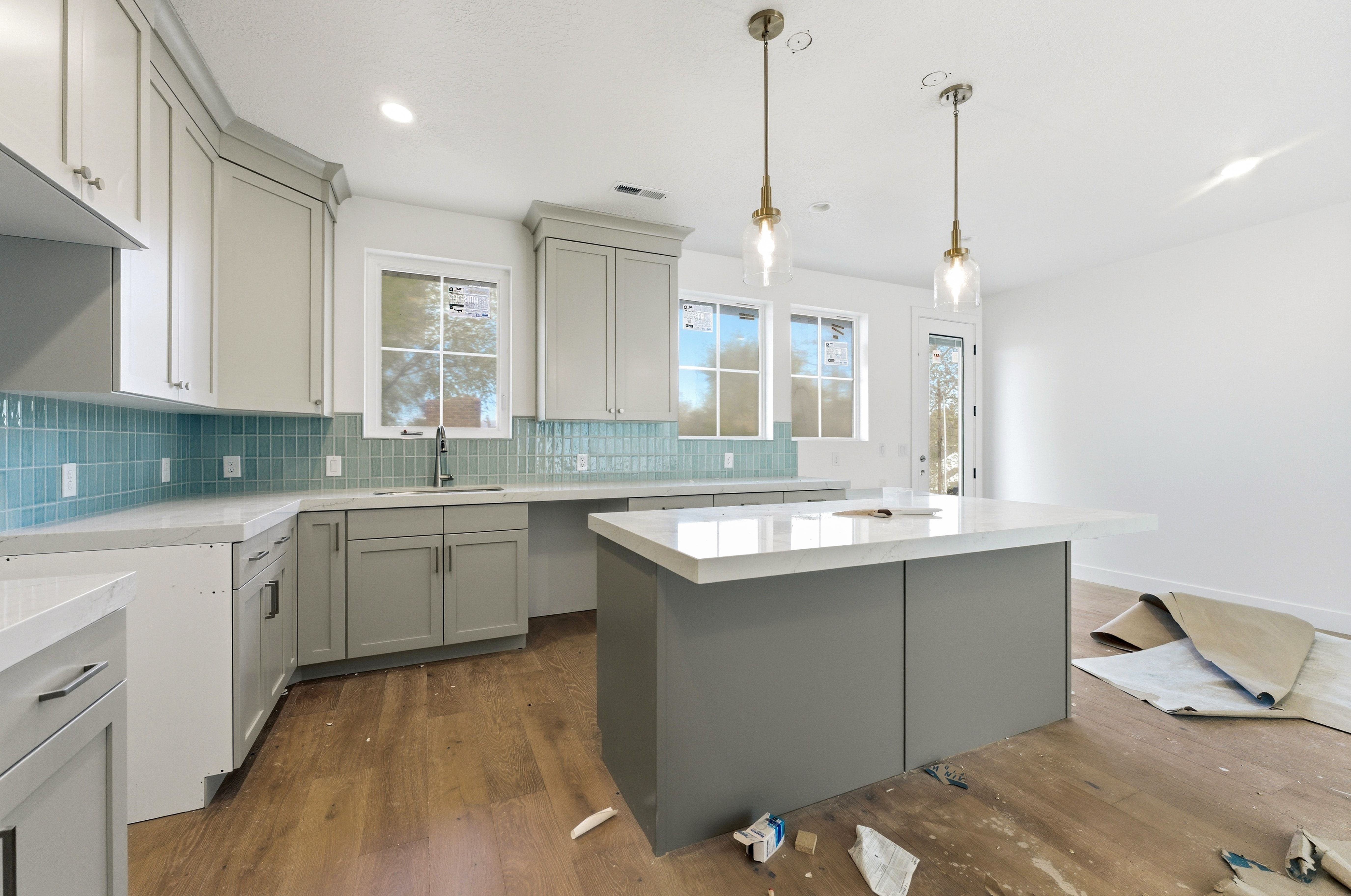 Kitchen with dark wood-style floors, a center island, hanging light fixtures, backsplash, and light stone counters