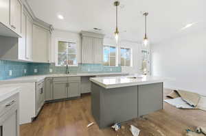 Kitchen with dark wood-style floors, a center island, hanging light fixtures, backsplash, and light stone counters