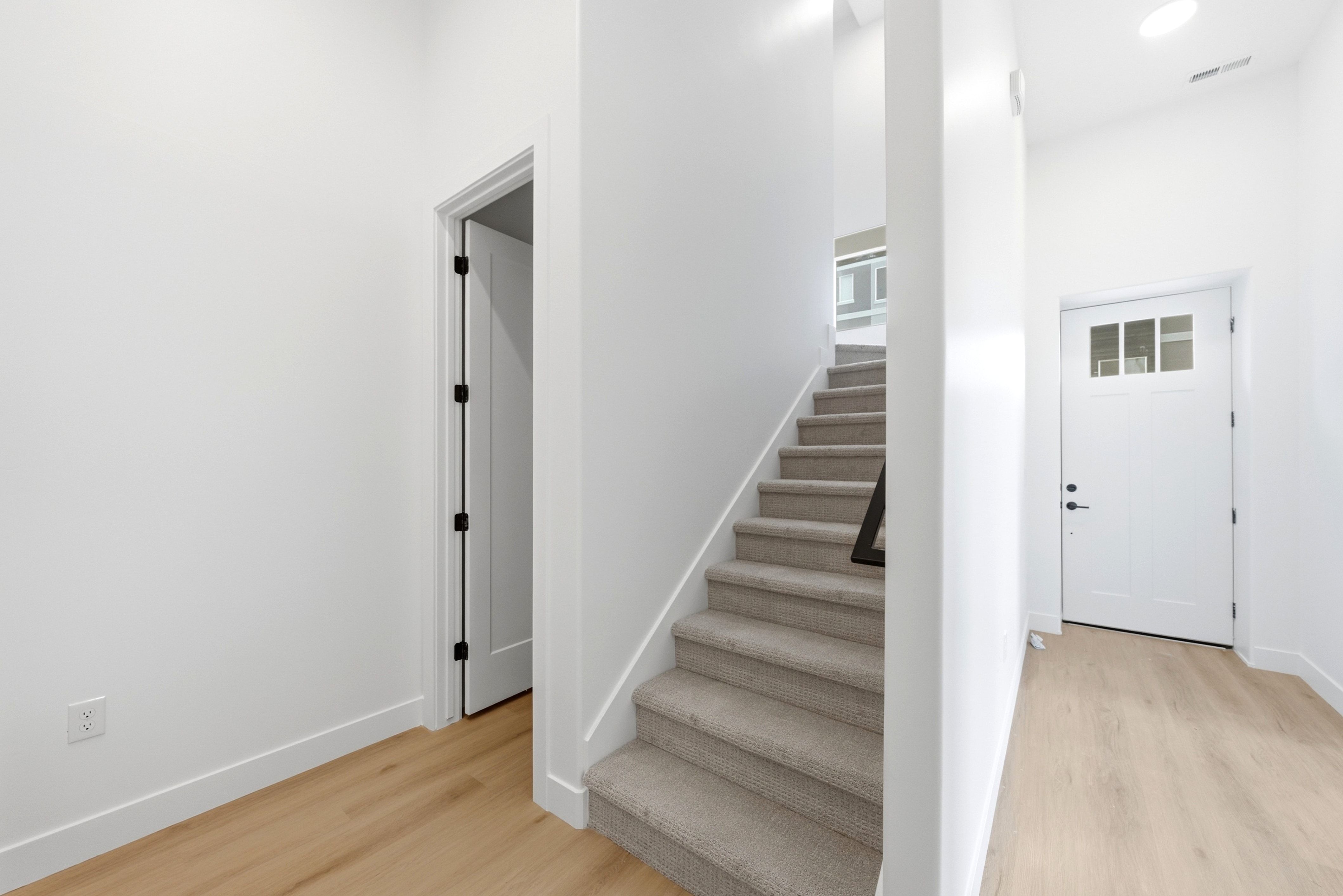 Entryway featuring wood-finish flooring, a white paneled door with glass inserts, and a carpeted staircase with a black handrail
