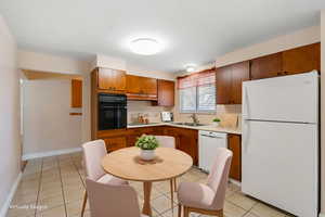 Kitchen featuring white appliances, light countertops, light tile patterned floors, and brown cabinetry
