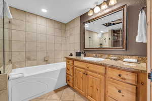 Full bath featuring vanity, a garden tub, light tile patterned floors, tile walls, and a stall shower