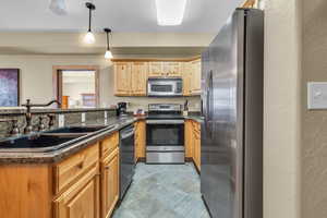 Kitchen featuring a textured wall, appliances with stainless steel finishes, decorative light fixtures, dark stone countertops, and light brown cabinetry