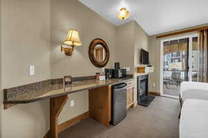 Kitchen featuring a fireplace with flush hearth, dark stone counters, stainless steel refrigerator, dark colored carpet, and a textured wall