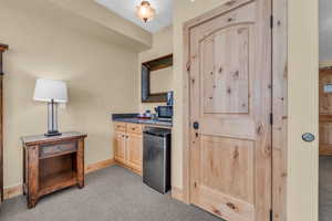 Kitchen with light brown cabinetry, light carpet, dark countertops, and fridge