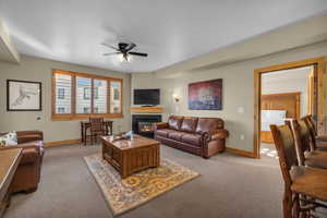 Living room with a ceiling fan, a glass covered fireplace, and light colored carpet