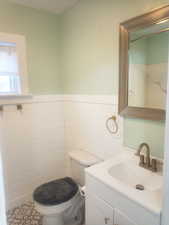 Half bath featuring vanity, wainscoting, and tile walls