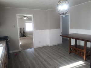 Unfurnished dining area featuring ceiling fan, wainscoting, wood finished floors, and crown molding