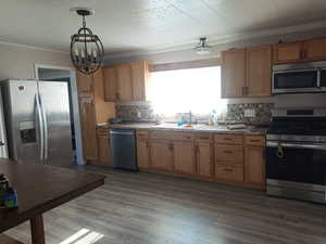 Kitchen featuring appliances with stainless steel finishes, decorative light fixtures, dark wood finished floors, a chandelier, and crown molding