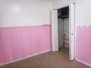 Unfurnished bedroom with a closet, light carpet, and a wainscoted wall