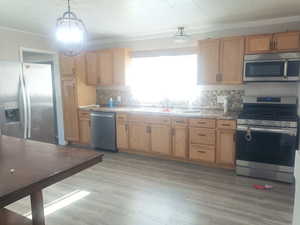 Kitchen featuring stainless steel appliances, pendant lighting, dark wood-type flooring, ornamental molding, and backsplash