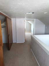 Hallway with a textured ceiling, light carpet, and lofted ceiling