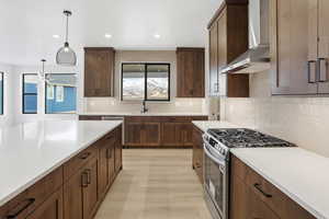 Kitchen with appliances with stainless steel finishes, wall chimney range hood, decorative light fixtures, decorative backsplash, and light wood finished floors