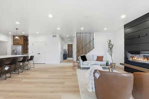 Living room with light wood-type flooring, stairs, recessed lighting, and a glass covered fireplace