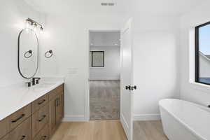 Full bathroom with a freestanding tub, vanity, and light wood-style flooring