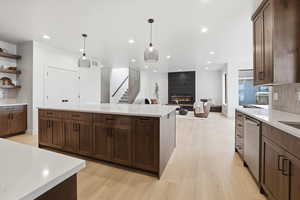 Kitchen with decorative backsplash, light stone countertops, a center island, dark brown cabinetry, and open floor plan