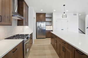 Kitchen featuring appliances with stainless steel finishes, wall chimney range hood, open shelves, light wood-style floors, and pendant lighting