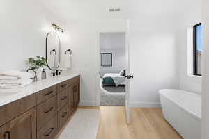 Full bath featuring a freestanding tub, double vanity, light wood finished floors, and ensuite bathroom
