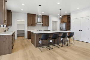 Kitchen with pendant lighting, a breakfast bar area, a center island, light wood-style flooring, and light stone countertops