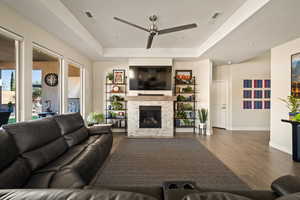 Living area with wood finished floors, a ceiling fan, a fireplace, a raised ceiling, and recessed lighting