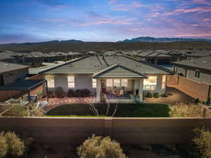 Back of house at dusk featuring a patio area, a mountain view, stucco siding, a fenced backyard, and a residential view