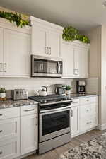 Kitchen with stainless steel appliances, white cabinets, dark stone countertops, backsplash, and light wood-style floors