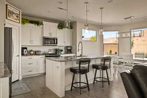 Kitchen with hanging light fixtures, dark stone countertops, white cabinetry, a center island with sink, and stainless steel appliances