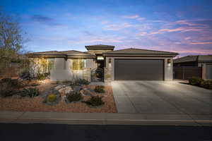 Prairie-style house with a gate, stone siding, stucco siding, an attached garage, and concrete driveway