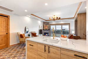 Kitchen featuring light stone counters, a raised ceiling, a brick fireplace, light brown cabinetry, and recessed lighting