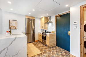 Kitchen featuring stainless steel appliances, tasteful backsplash, wall chimney exhaust hood, light brown cabinetry, and recessed lighting